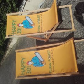 Zwei gelbe Sonnenliegen mit dem Logo der KUBA STEFAN Baumschlägerung u. -bringung